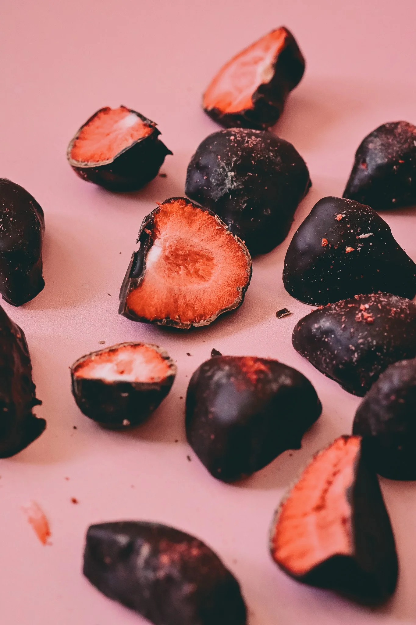 Gros plan de prunes noires avec leur chair rouge orangée, quelques prunes coupées en deux sur un fond rose clair.