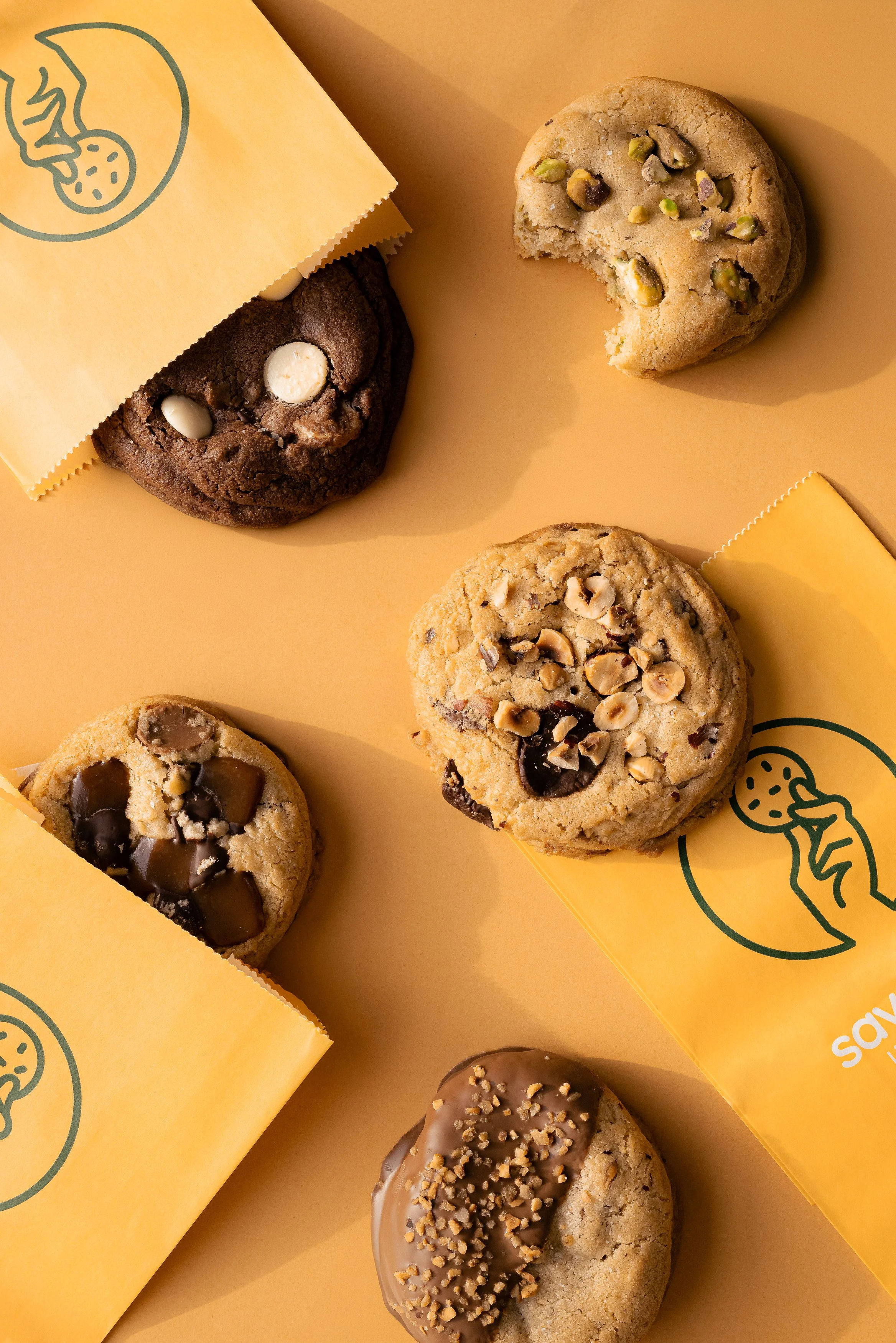 Gâteaux avec différents types de garnitures, y compris des noix, du chocolat et des pistaches, emballés dans des papiers de couleur orange avec un logo de biscuit.