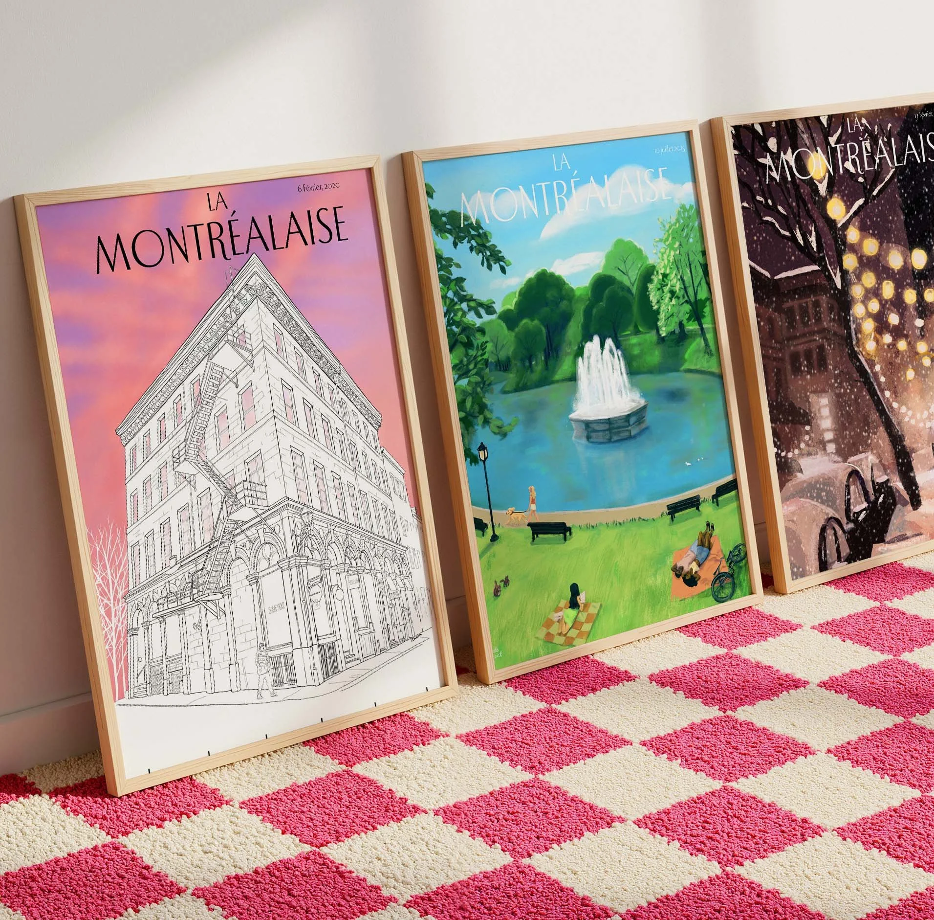 Trois affiches artistiques encadrées posées contre un mur, représentant des scènes de Montréal, avec un tapis rayé rose et beige au sol.