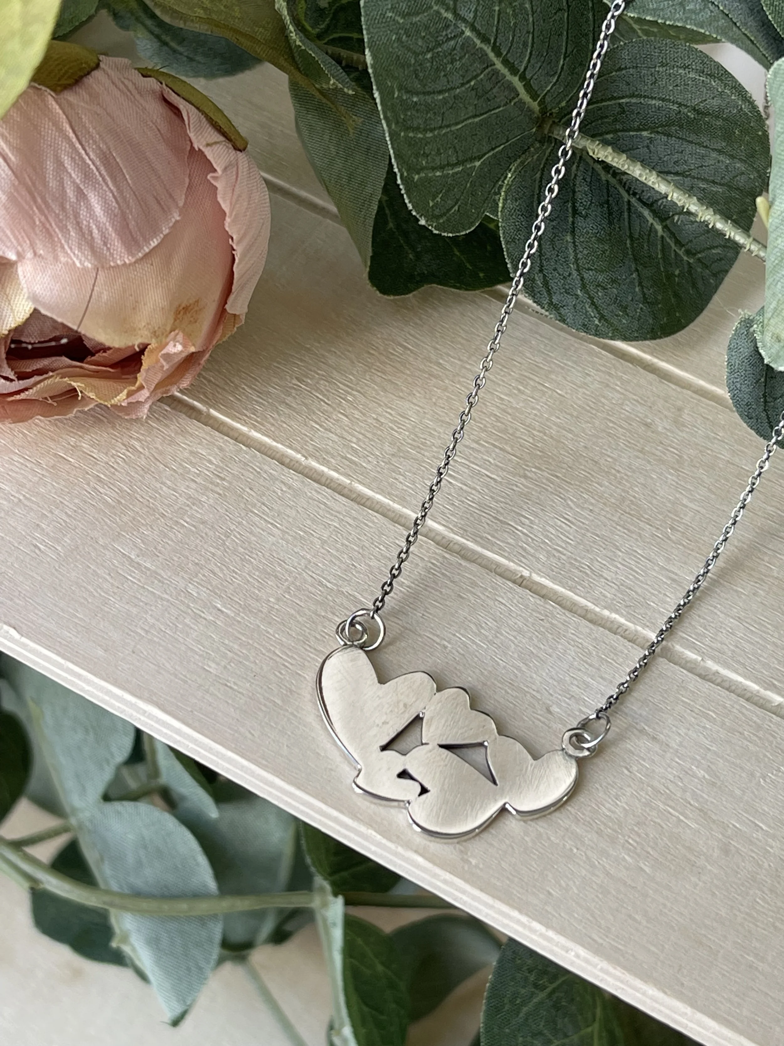 Collier en argent avec pendentif en forme de papillon, posé sur une surface en bois, entouré de feuilles vertes