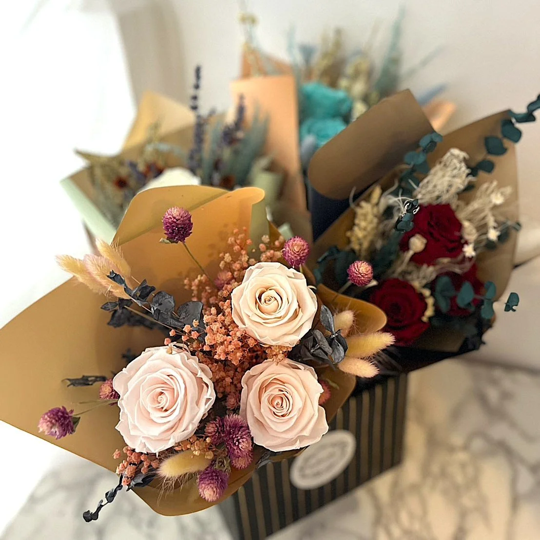 Bouquet de fleurs avec des roses blanches, des fleurs roses et d'autres variétés dans un emballage en papier marron.