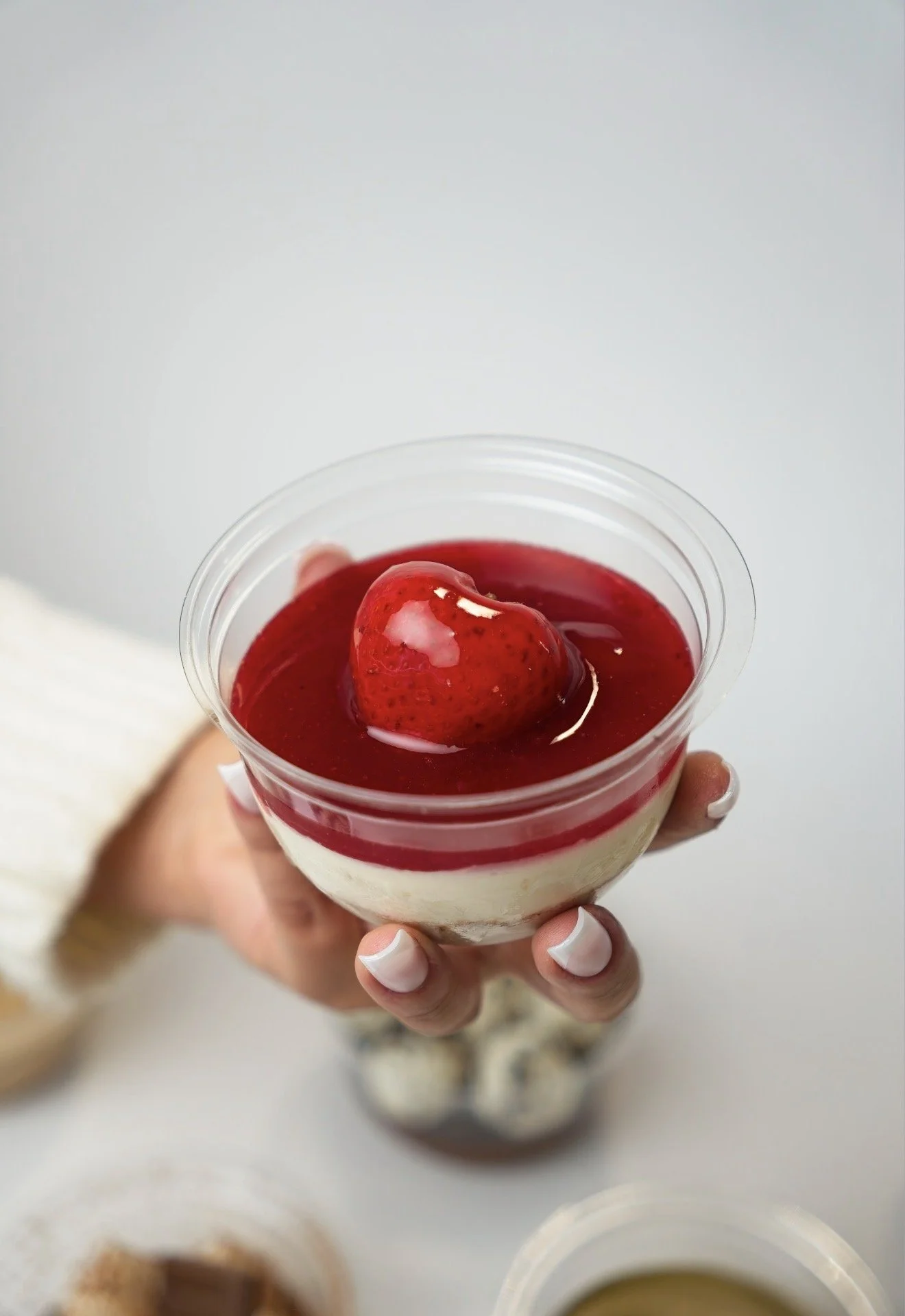 Un dessert en coupe, avec une couche de crème et des fruits rouges, notamment une fraise en garniture.