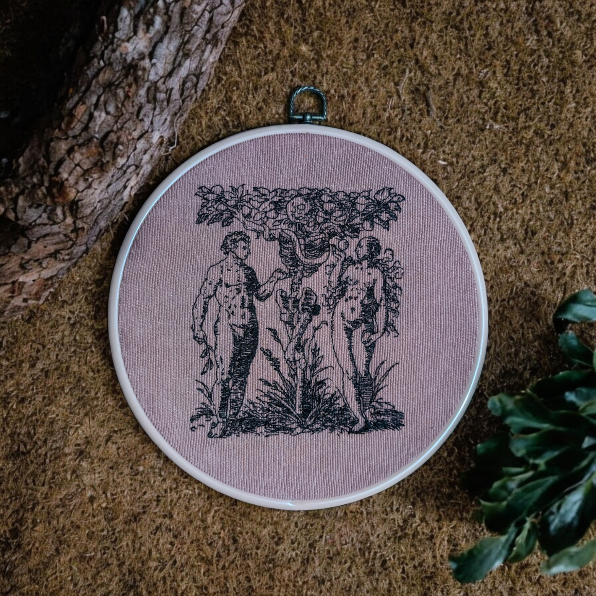 Une pièce de broderie représentant un bûcheron avec une hache, située dans une assiette sur une surface en terre ou céramique, à côté d'un arbre ou d'une branche.