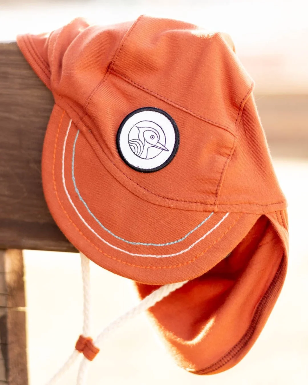 Casquette orange avec un logo de plongeur ou de têtard, suspendue à une surface en bois.