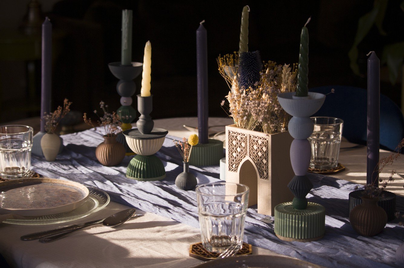 Une table décorée avec des bougies, des vases avec des fleurs séchées, des assiettes en porcelaine et des verres en cristal, dans un style élégant et moderne.