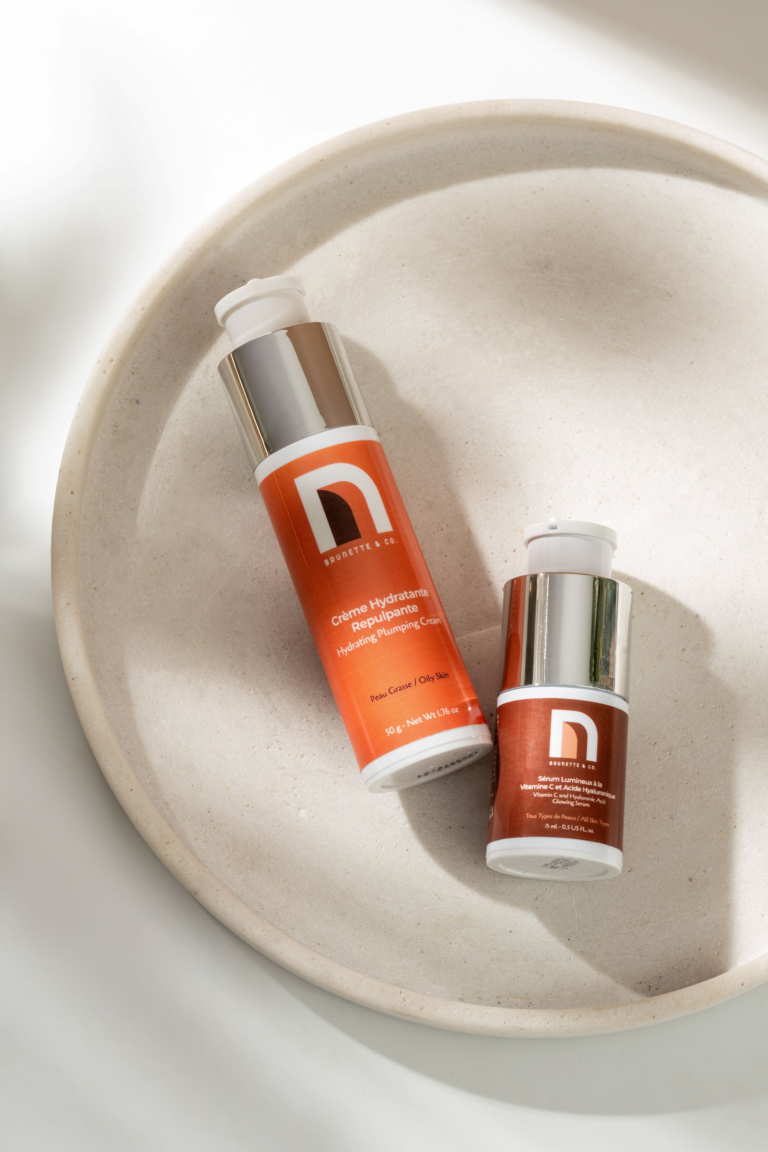 Deux tubes de sérum hydratant et lumineux pour la peau grasse dans un bol beige.