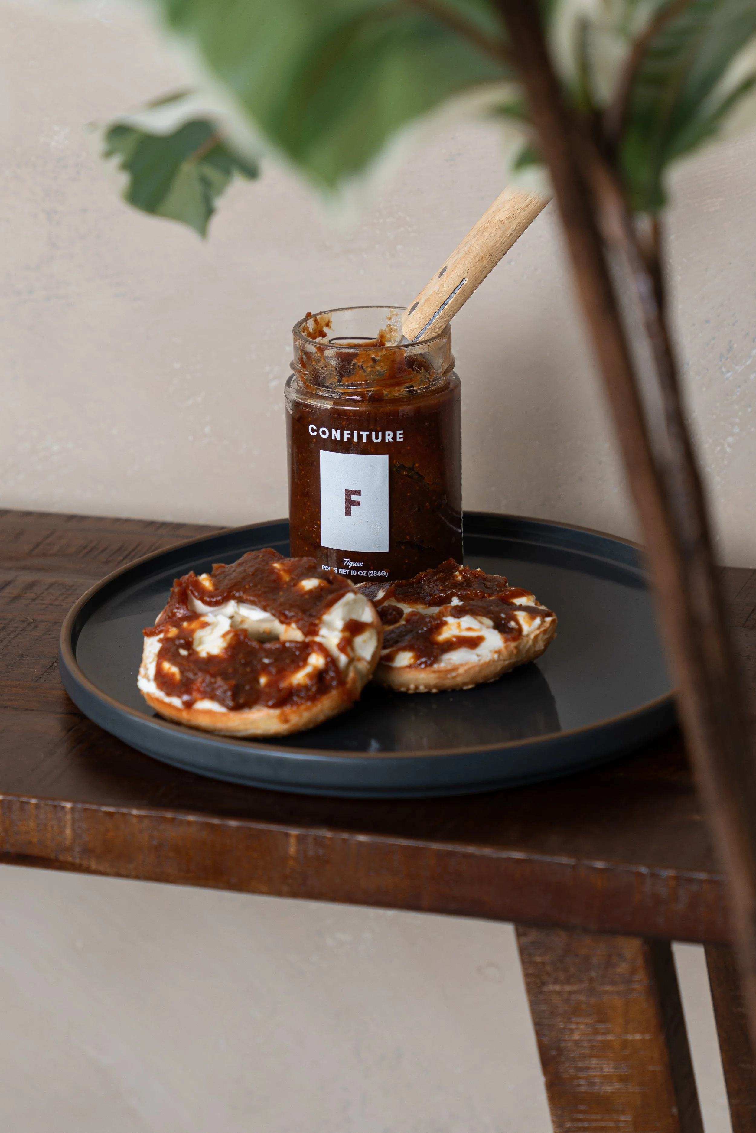 Une boîte de confiture à la figue sert à étaler de la confiture sur des tranches de pain ou des biscuits, placée sur une assiette noire à côté.