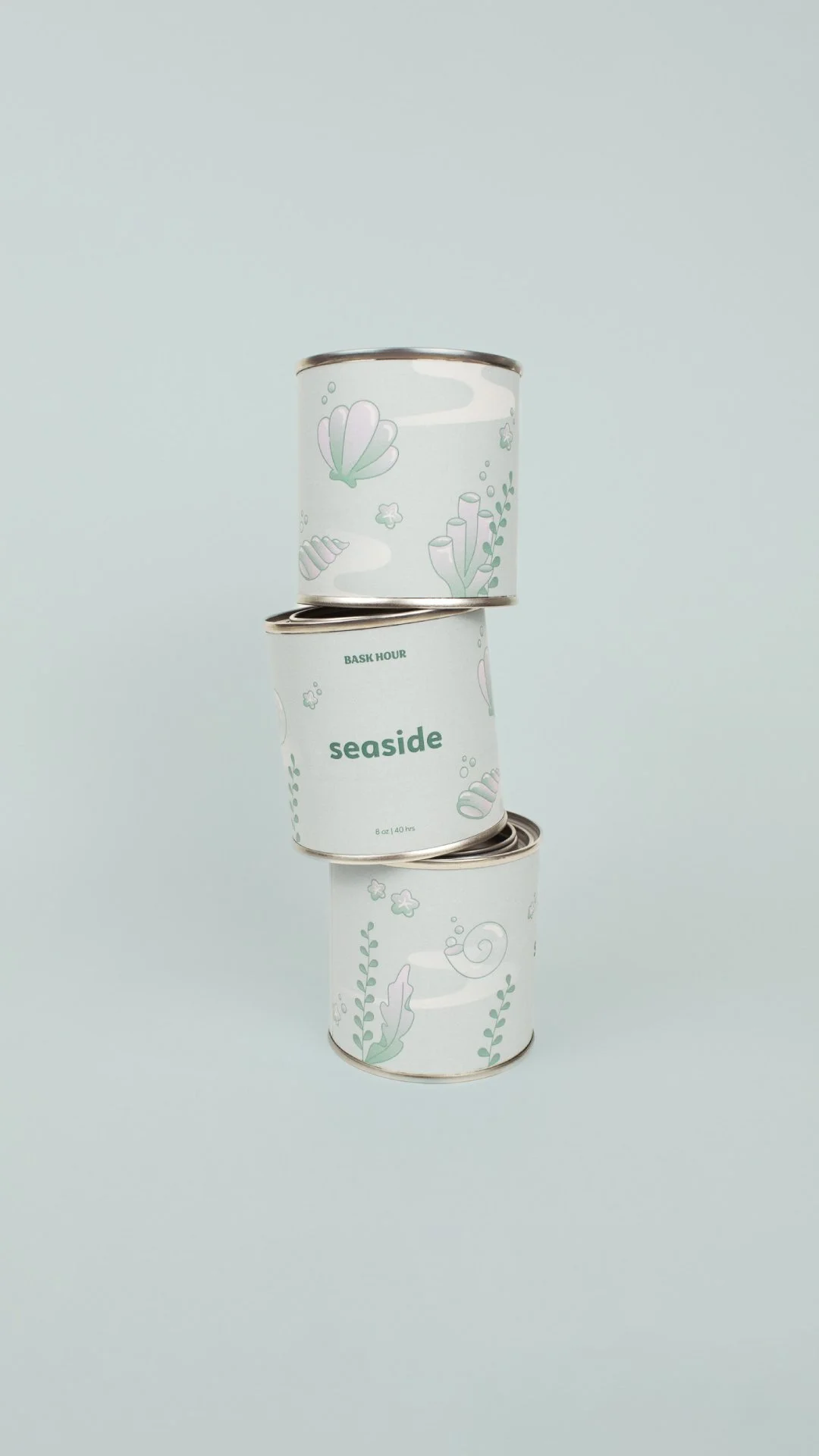 Trois boîtes de conserve empilées verticalement avec une conception minimaliste de style marine, comprenant des illustrations de coquillages, de coraux, d'algues et d'autres éléments sous-marins. La boîte du milieu affiche le mot 'seaside' et indique une capacité de 8 oz ou 40 hrs.
