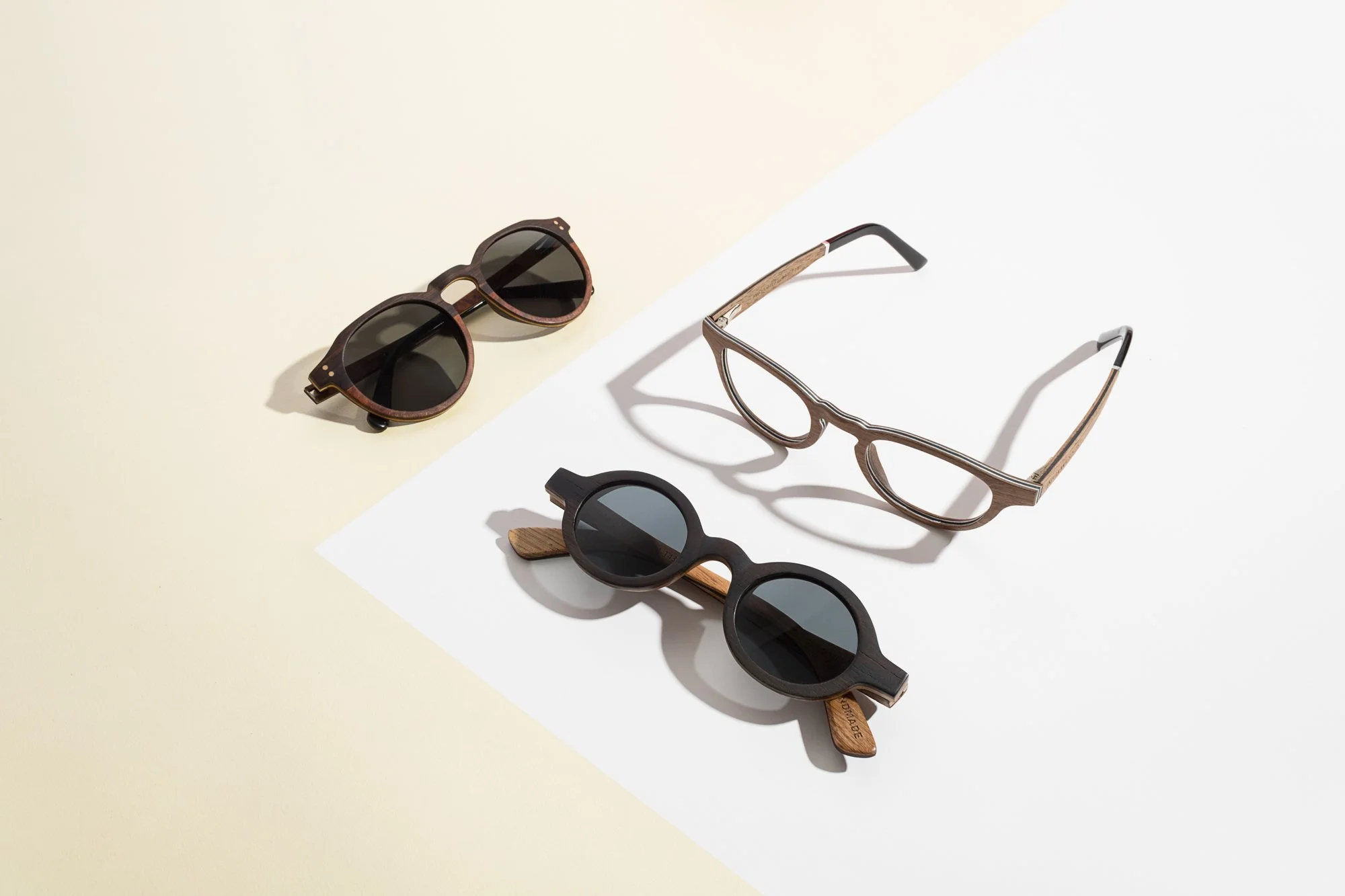 Quatre paires de lunettes de soleil posées sur une surface divisée en deux couleurs, crème et blanc, avec des ombres portées.