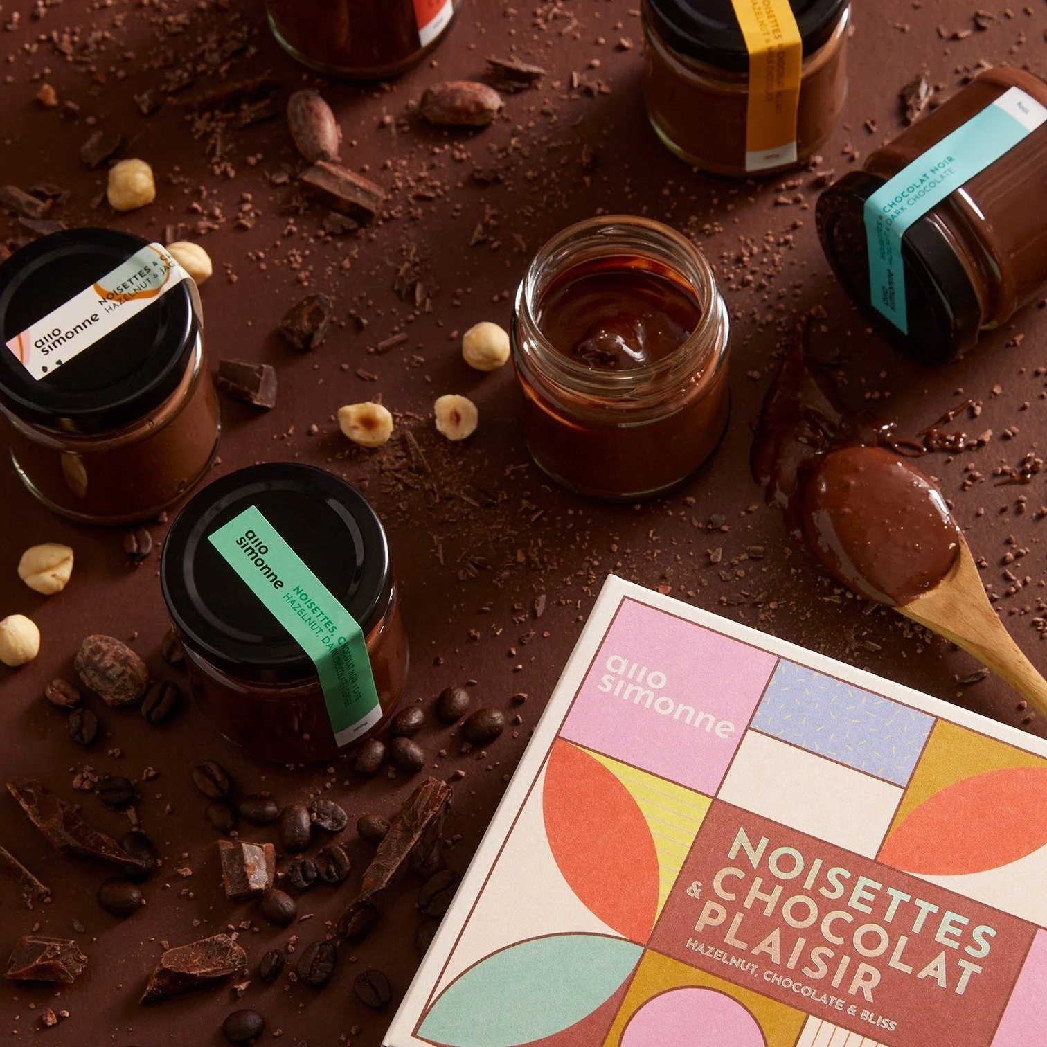 Pot de chocolat, éclats de chocolat, graines de café et noisettes sur une surface en bois, avec un livre intitulé 'Noisettes & Chocolat Plaisir'.