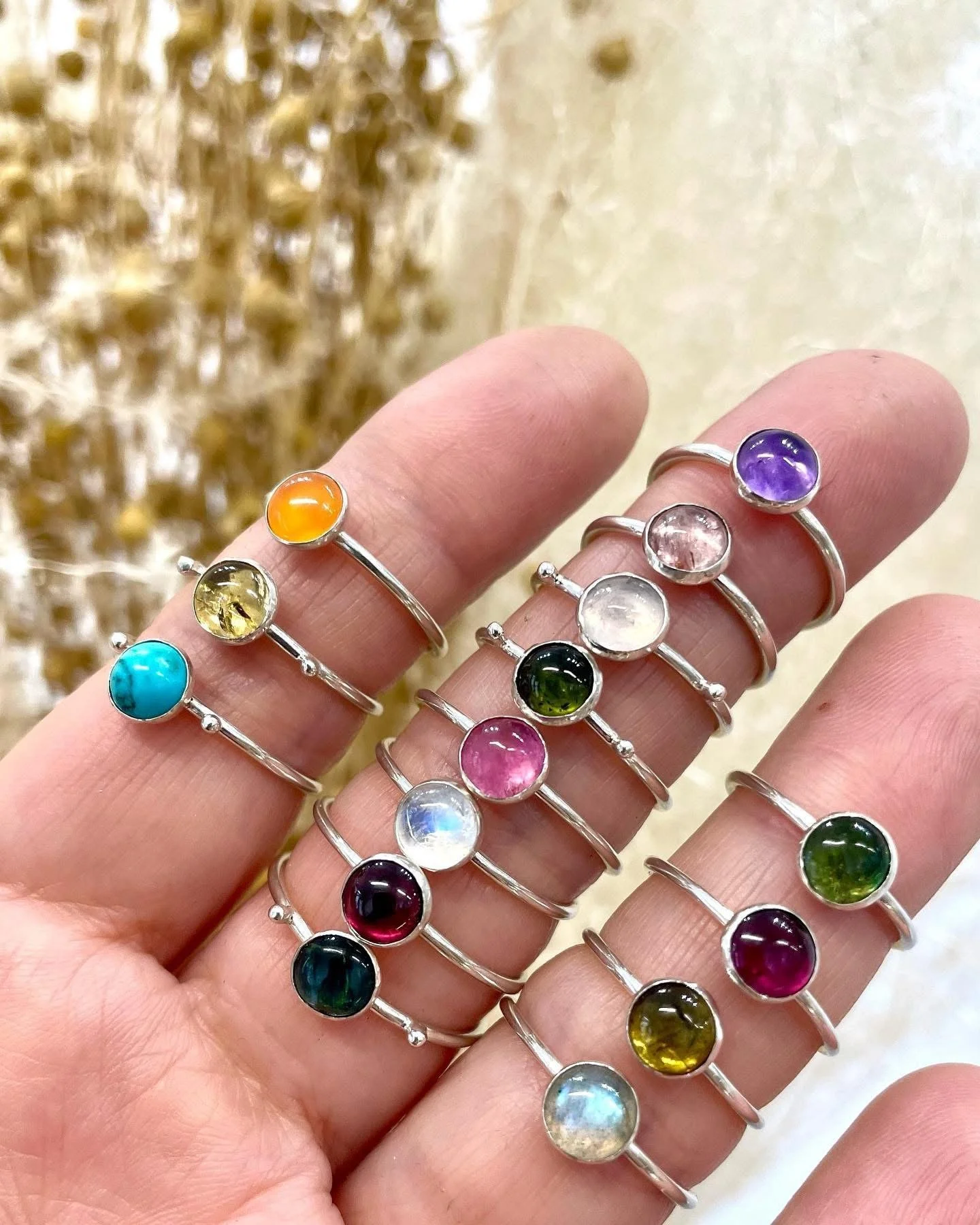 Main tenant plusieurs bagues en argent, chacune ornée d'une pierre précieuse ou semi-précieuse de différentes couleurs, avec un fond flou.