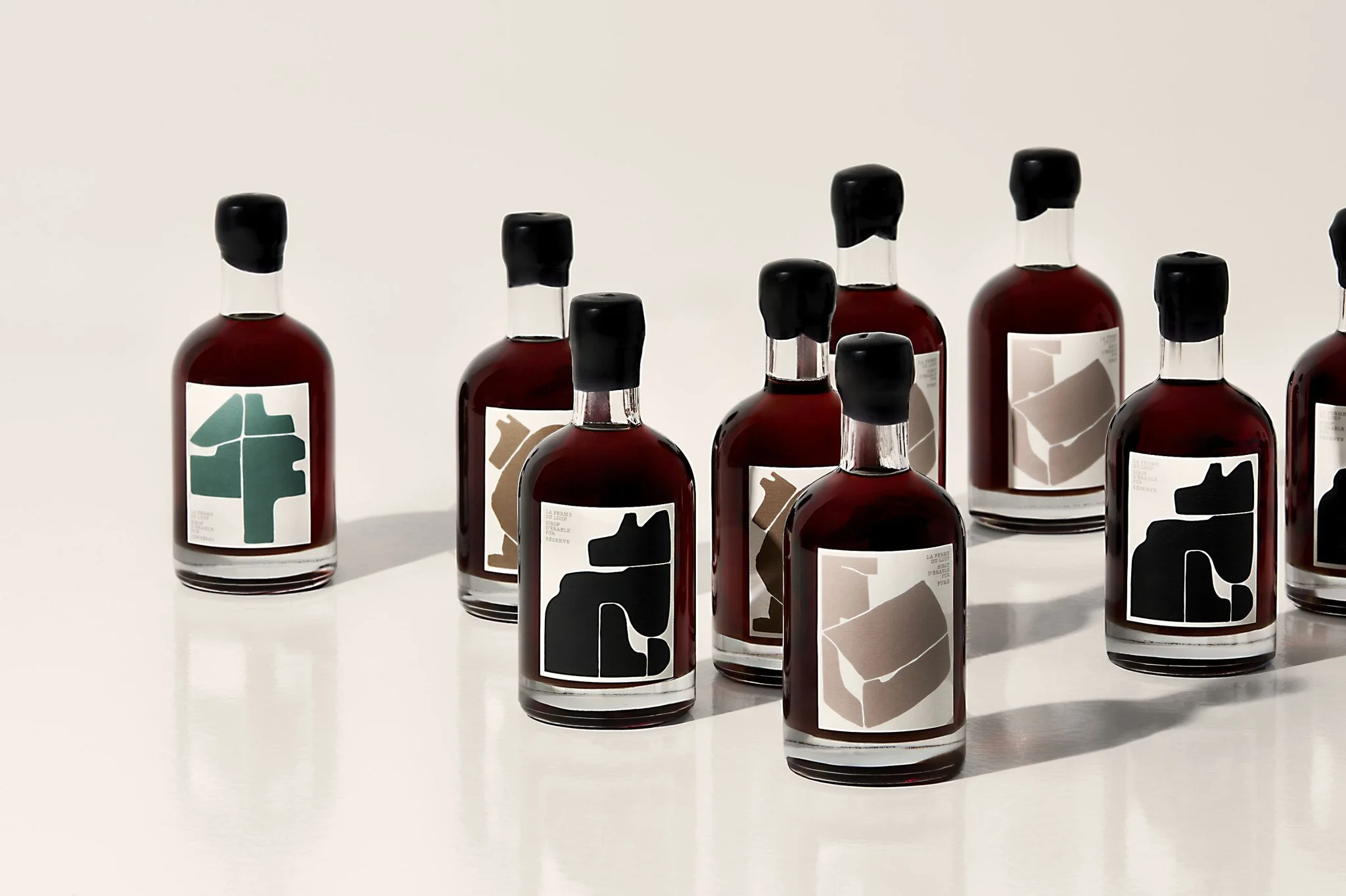 Des bouteilles de couleur rouge foncé avec des étiquettes modernes et minimalistes, alignées sur une surface blanche.