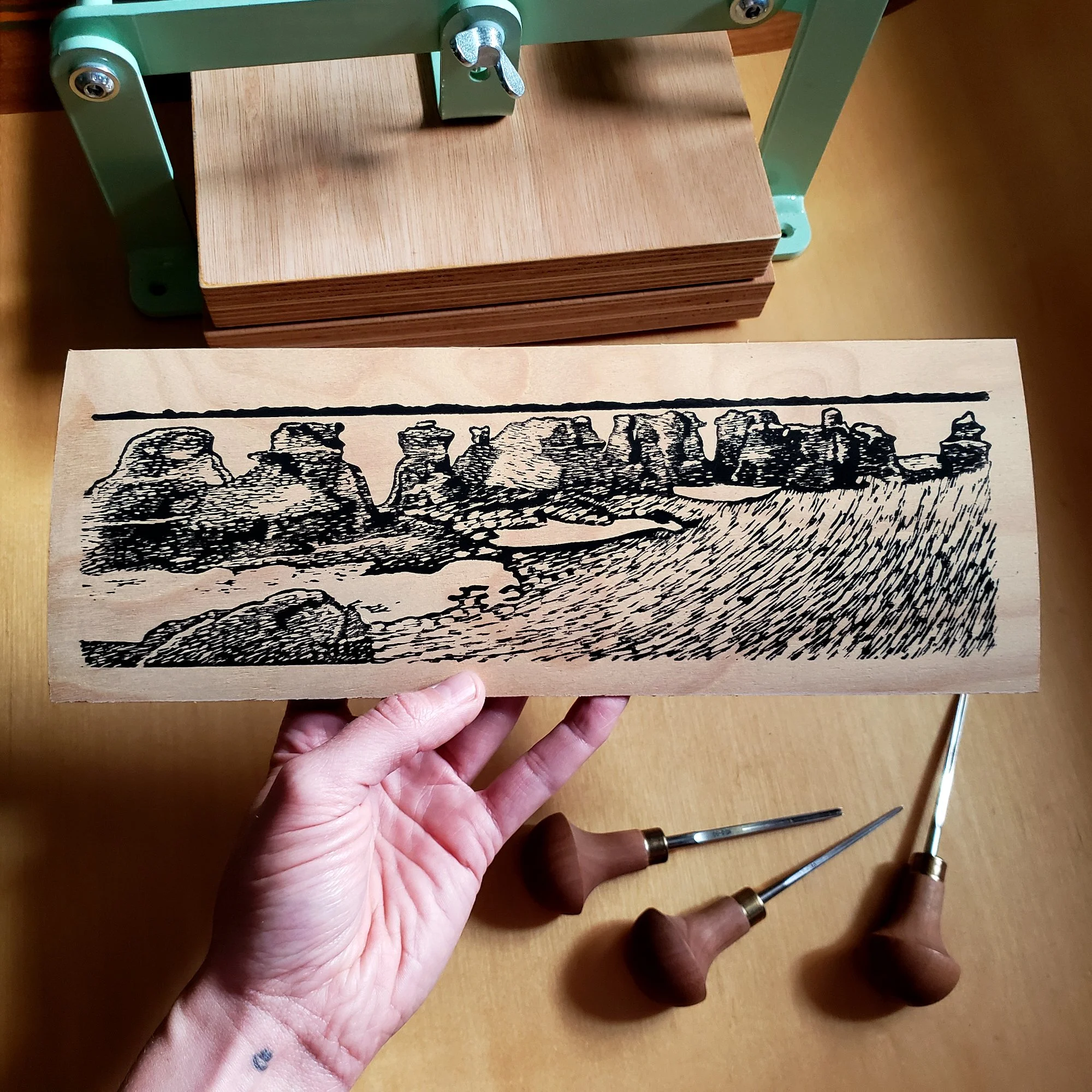 Une main tenant une planche en bois, avec à côté des outils en bois (un marteau et un burin).