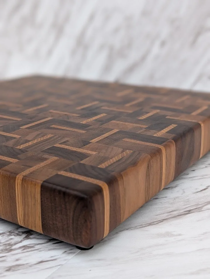 Planche à découper en bois avec motif géométrique en bois clair et foncé, reposant sur un surface en marbre blanc.
