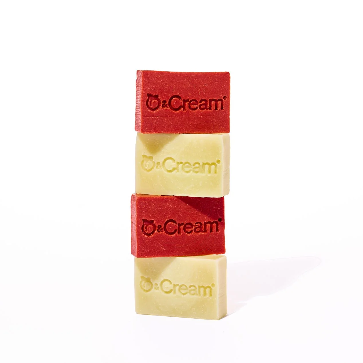 Quatre morceaux de savon, deux rouges et deux blancs, empilés en alternance, avec le texte '& Cream' gravé dessus, sur fond blanc.