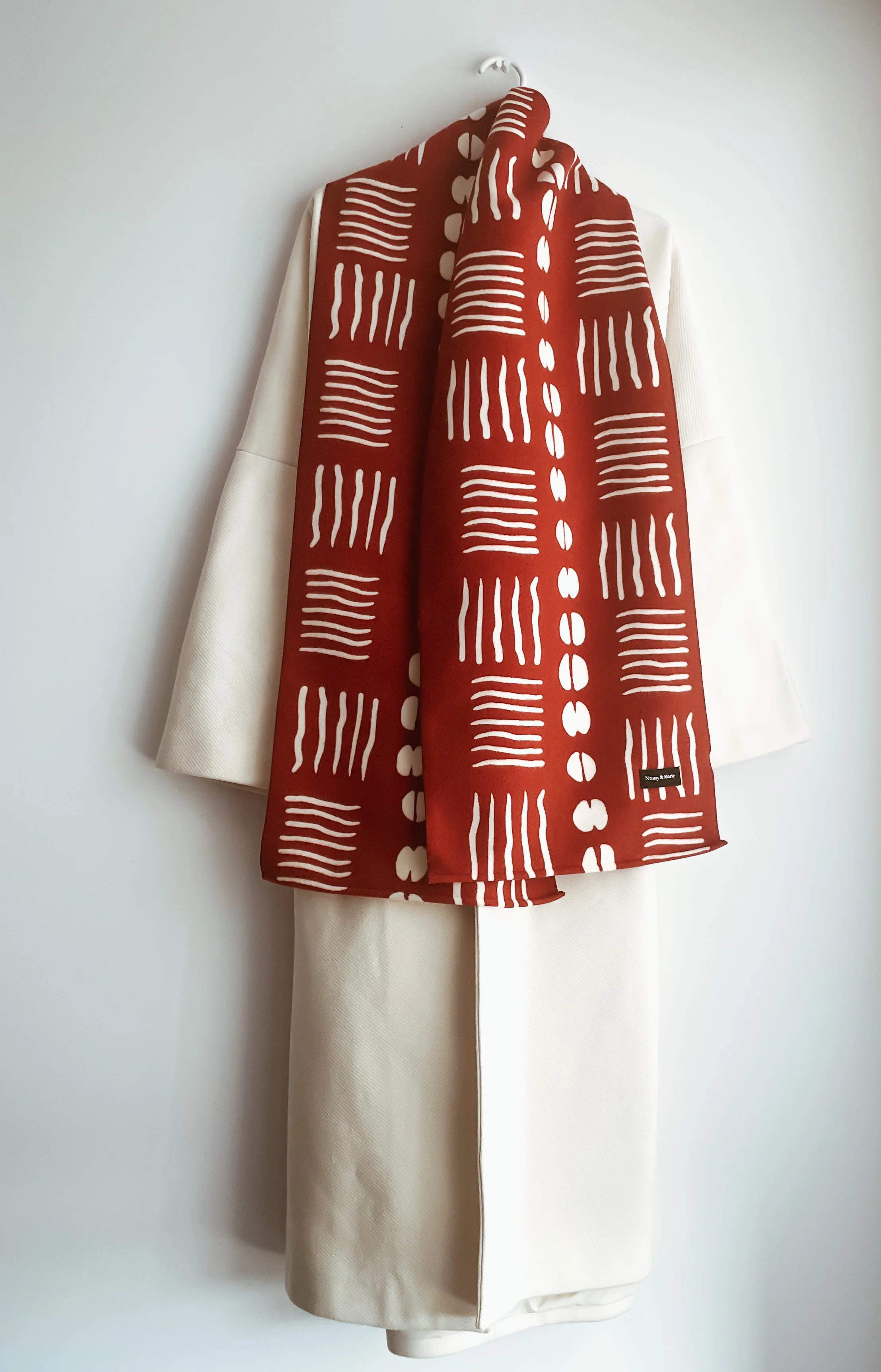 Veste blanche avec un foulard rouge à motifs blancs, suspendu à un crochet.