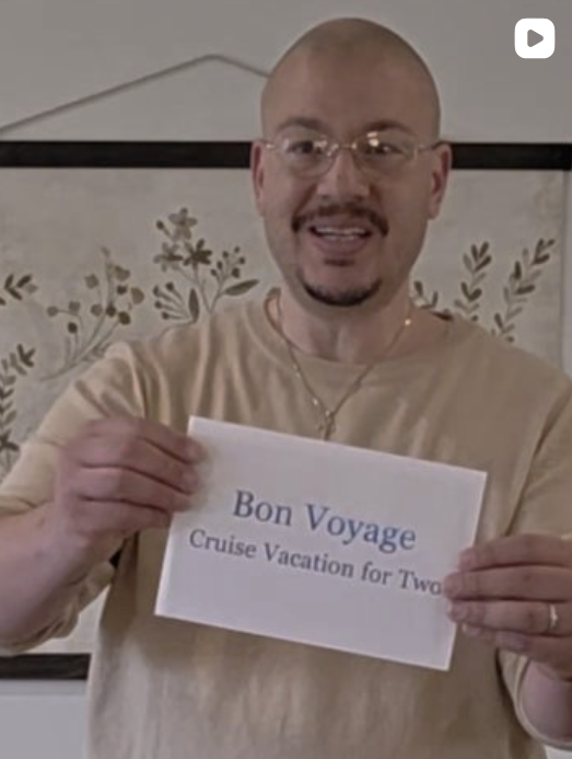 Man with glasses and a beige shirt holding a sign that reads "Bon Voyage Cruise Vacation for Two".