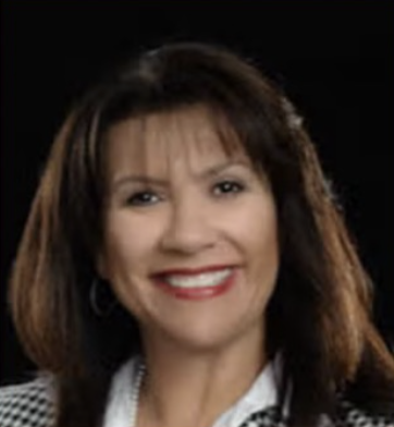 A woman with shoulder-length brown hair smiling, wearing a checkered blazer and white shirt, against a dark background.