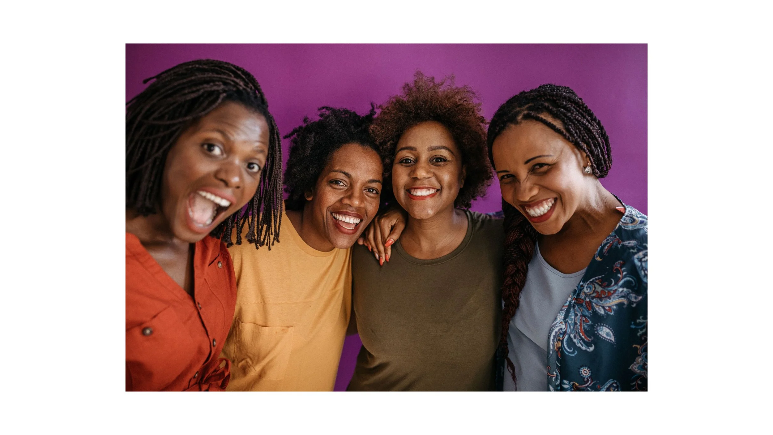 Group of four women smiling and embracing each other against a purple background.