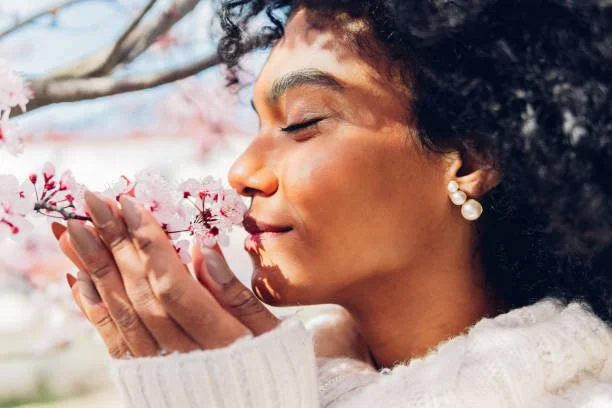 A woman with curly hair and pearl earrings smells pink cherry blossoms.