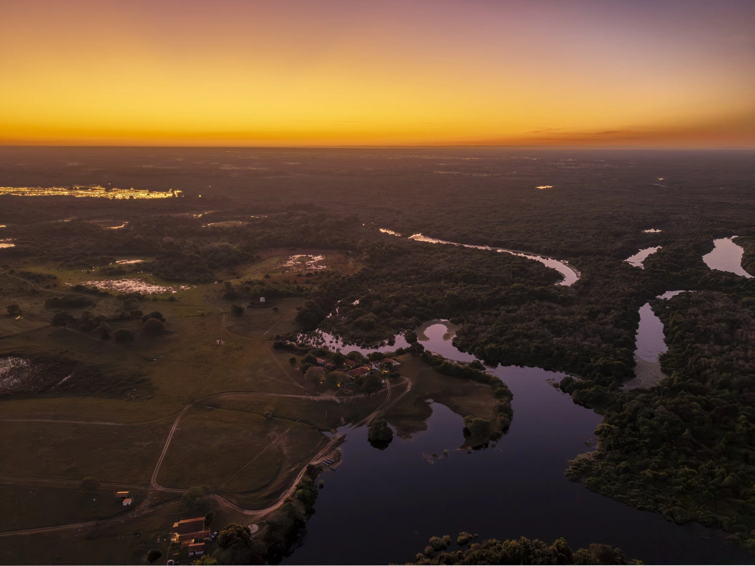 Aerial view of a river winding through a lush green landscape during sunset with a vibrant orange and purple sky.
