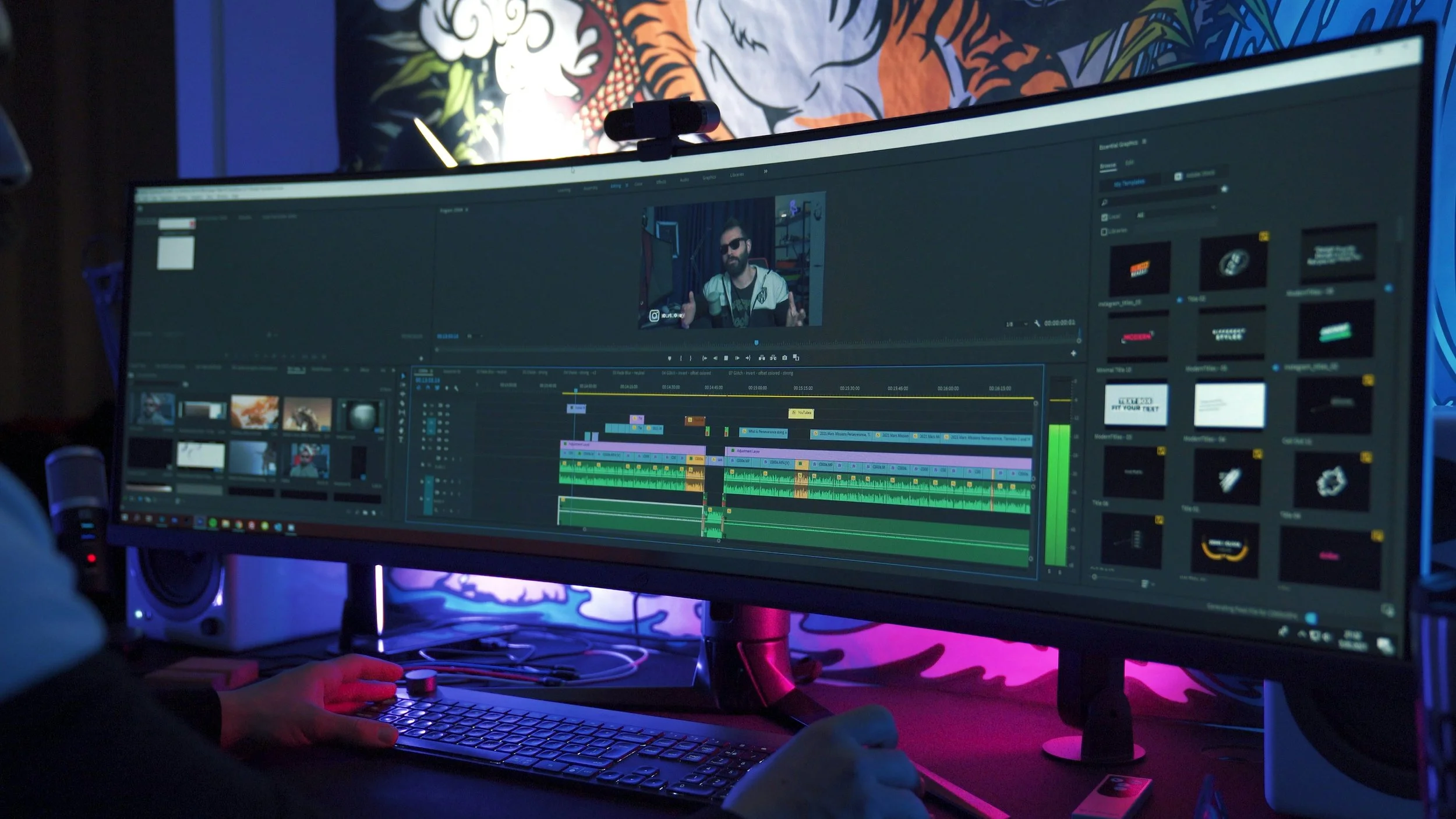 Editing a video on a large computer monitor displaying video editing software with multiple color-coded tracks and clips, in a dark room with colorful background art.