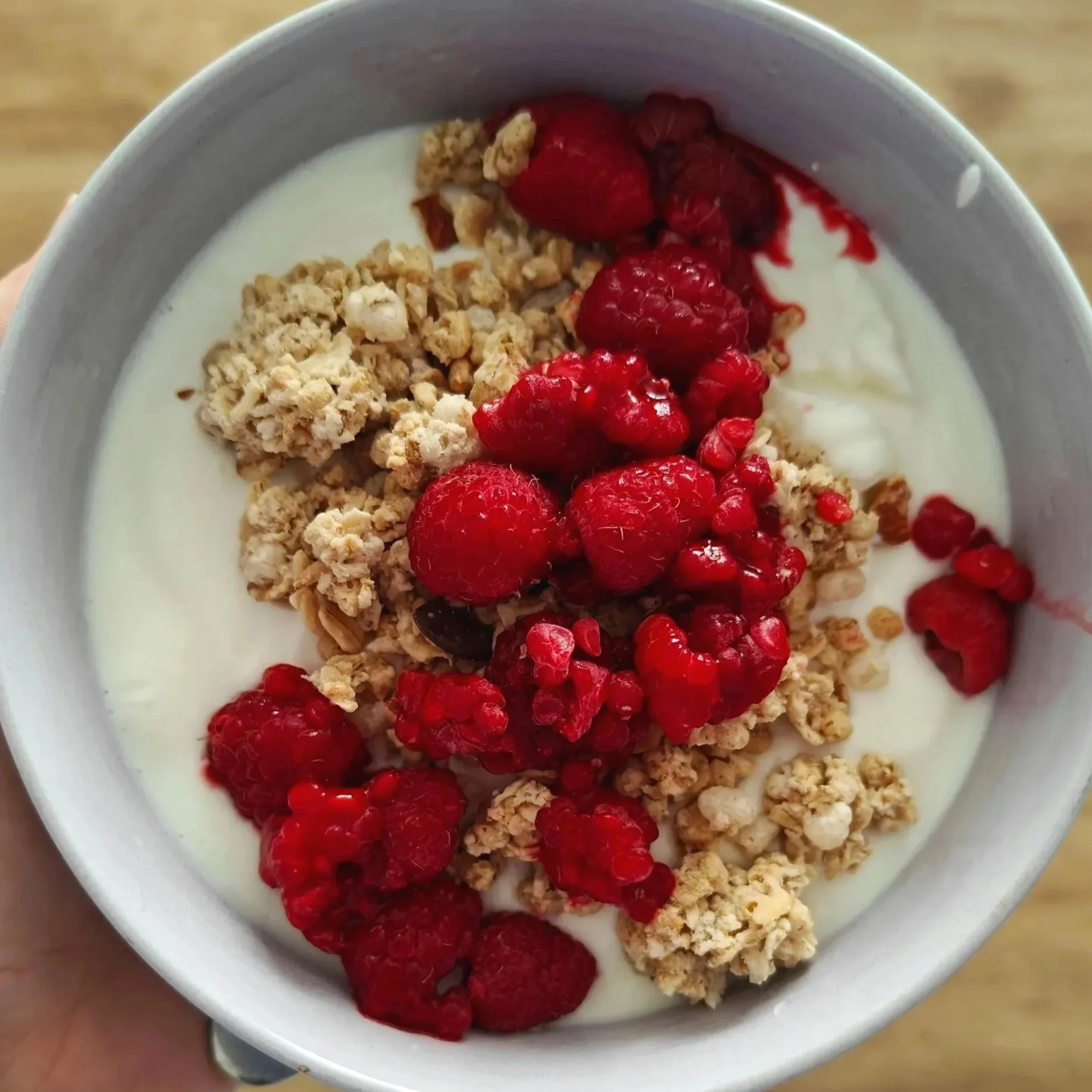 A white bowl containing yogurt topped with granola, red strawberries, and red raspberries.