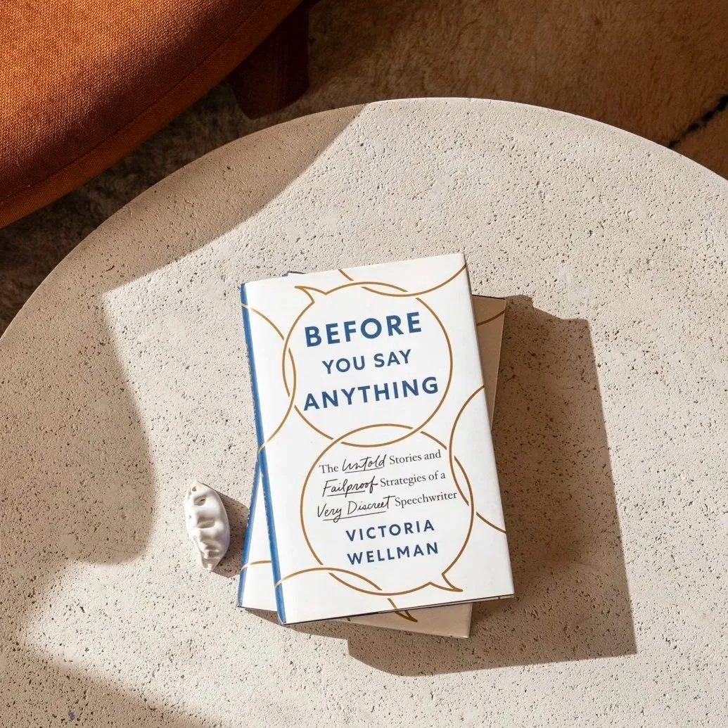 A book titled 'Before You Say Anything' by Victoria Wellman, published by St Martin's Press, resting on a round, textured beige table. Sunlight and shadow are visible across the table.