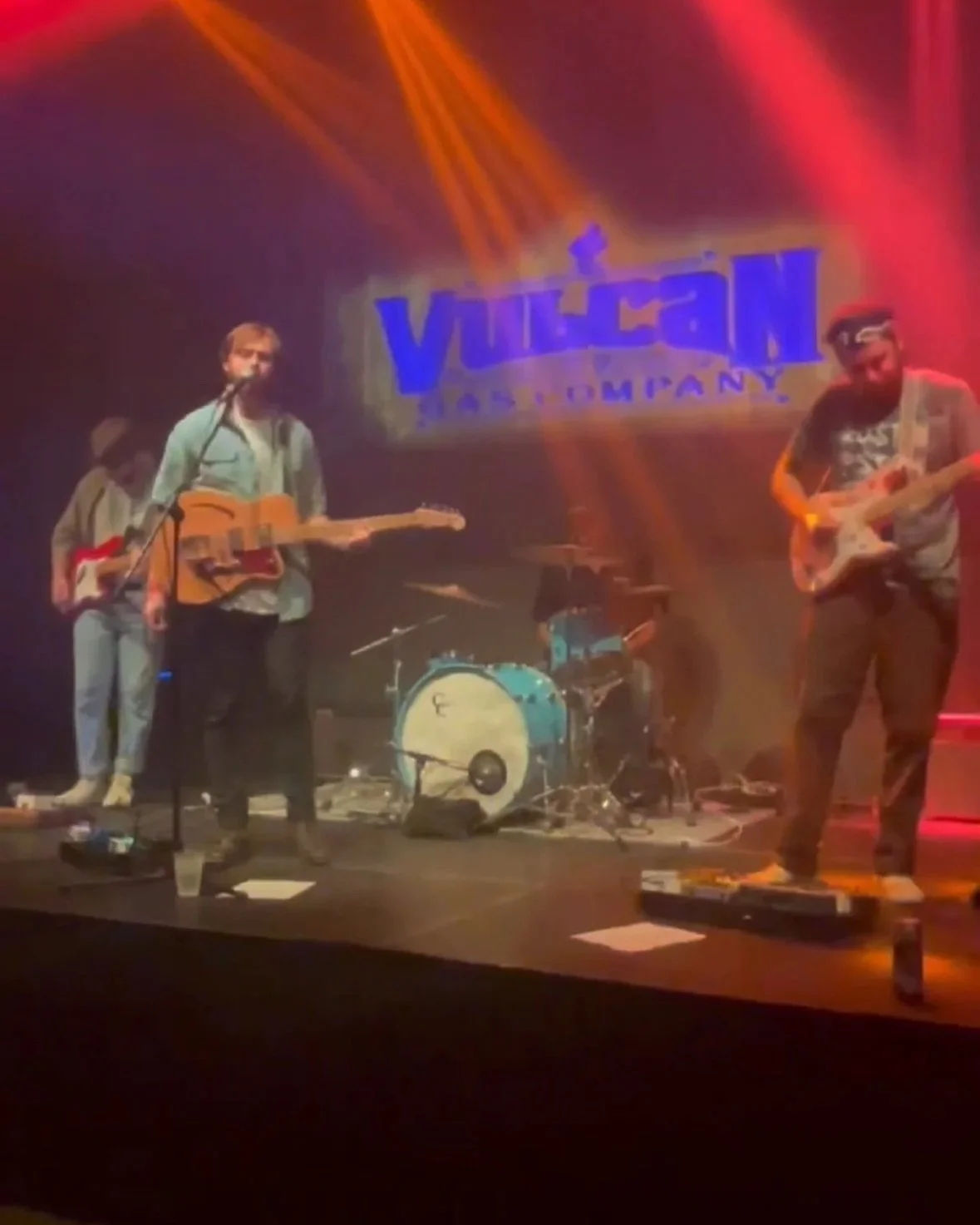 A band performing on stage with a sign in the background that reads 'Vulcan Gas Company'. The band includes a guitarist who is now playing shows in Minnesota. Bringing The Twin Cities his expertise in performance and event coordination.