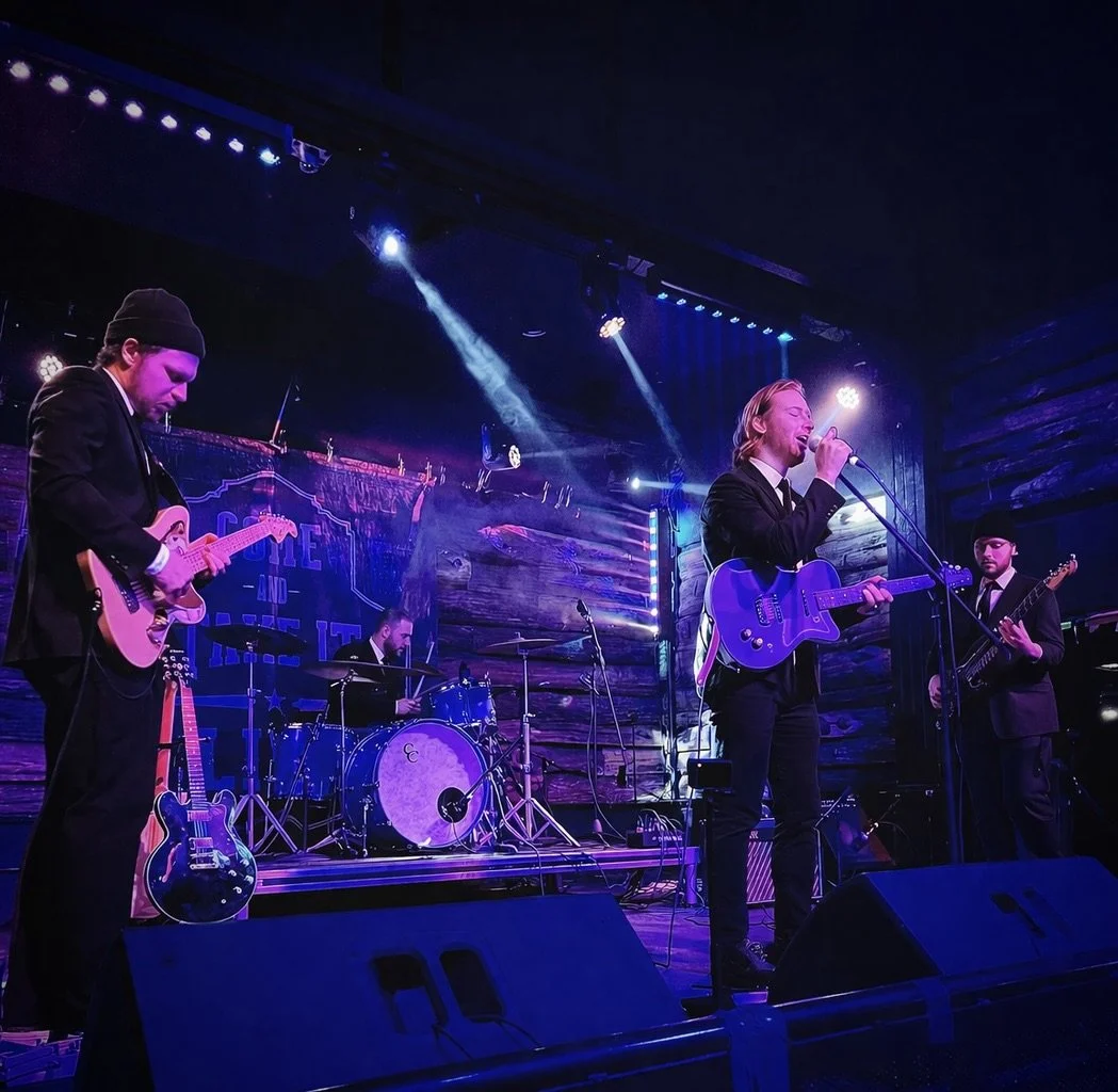 A four-member band performing on stage with purple and blue lighting, featuring a full band at a wedding. Playing weddings is an area of expertise for this very professional band in the Twin Cities.