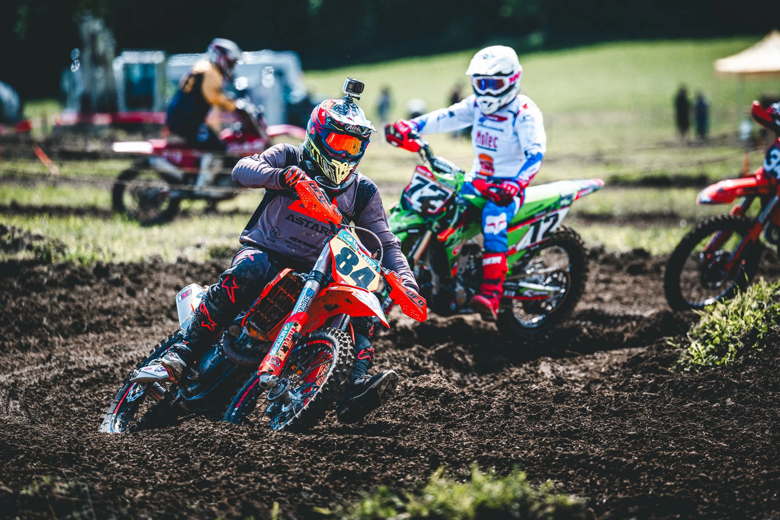 Ein KTM-Fahrer (Startnummer 84) führt ein enges Verfolgerfeld durch eine schlammige Kurve beim SAM-Rennen in Hünikon (Thurgau), packende Renn-Action aus der Ostschweiz.