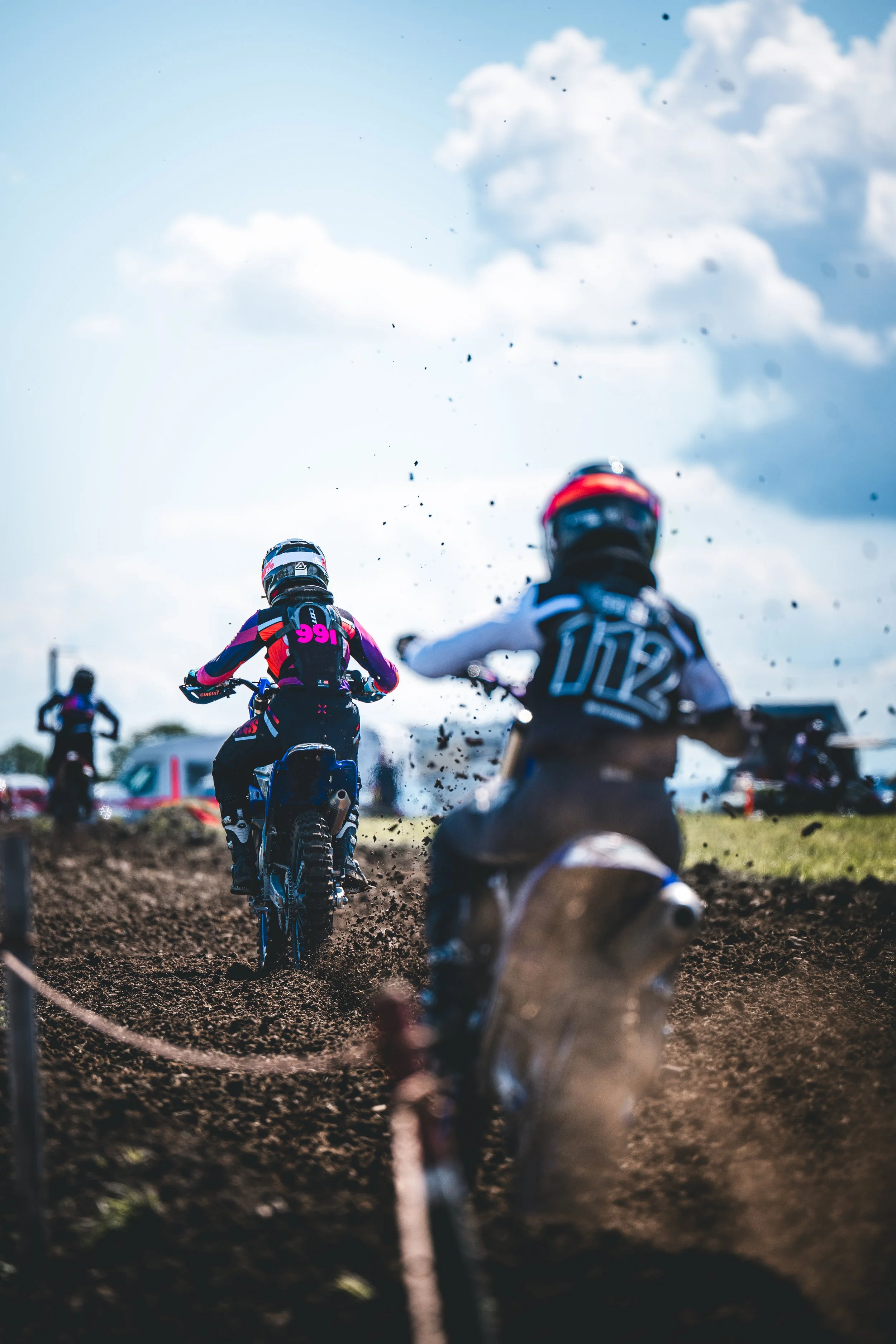 Dramatische Verfolgerperspektive im Hochformat: Motocross-Fahrer (Startnummer 112) beschleunigen auf der staubigen SAM-Rennstrecke in Hünikon (Thurgau), packende Sportfotografie aus der Ostschweiz.