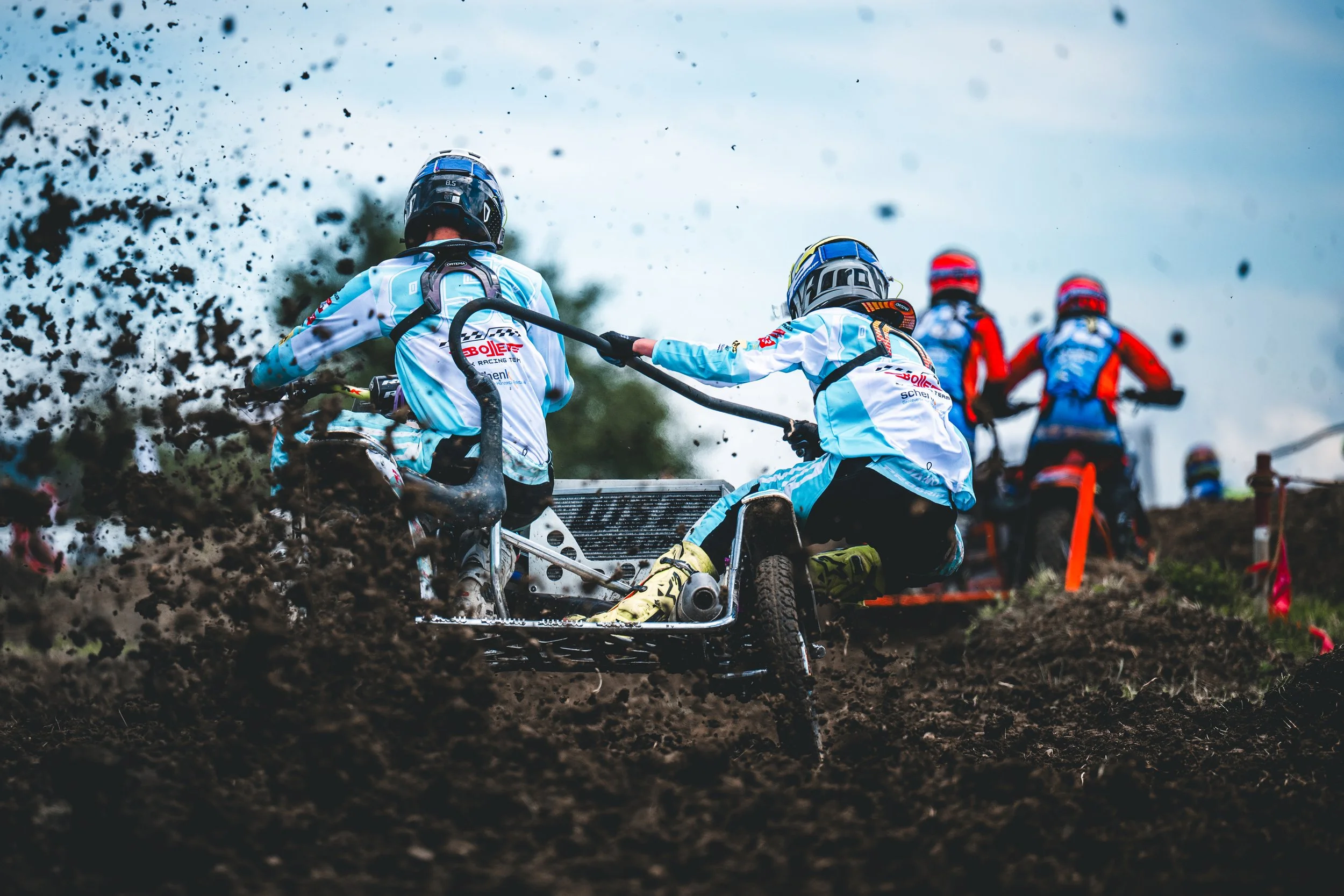 Spektakuläre Heckansicht eines hellblauen Motocross-Seitenwagen-Teams, das beim Beschleunigen eine massive Dreckwolke aufwirbelt, moody Sportreportage.