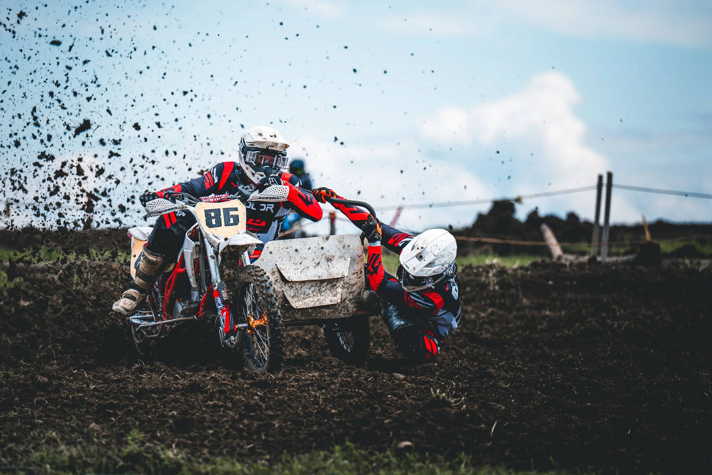 Ein rot-schwarzes Motocross-Gespann mit der Startnummer 86 kämpft sich durch eine tiefe Schlammkurve, dynamische Schweizer Sportfotografie im Cinematic-Look.