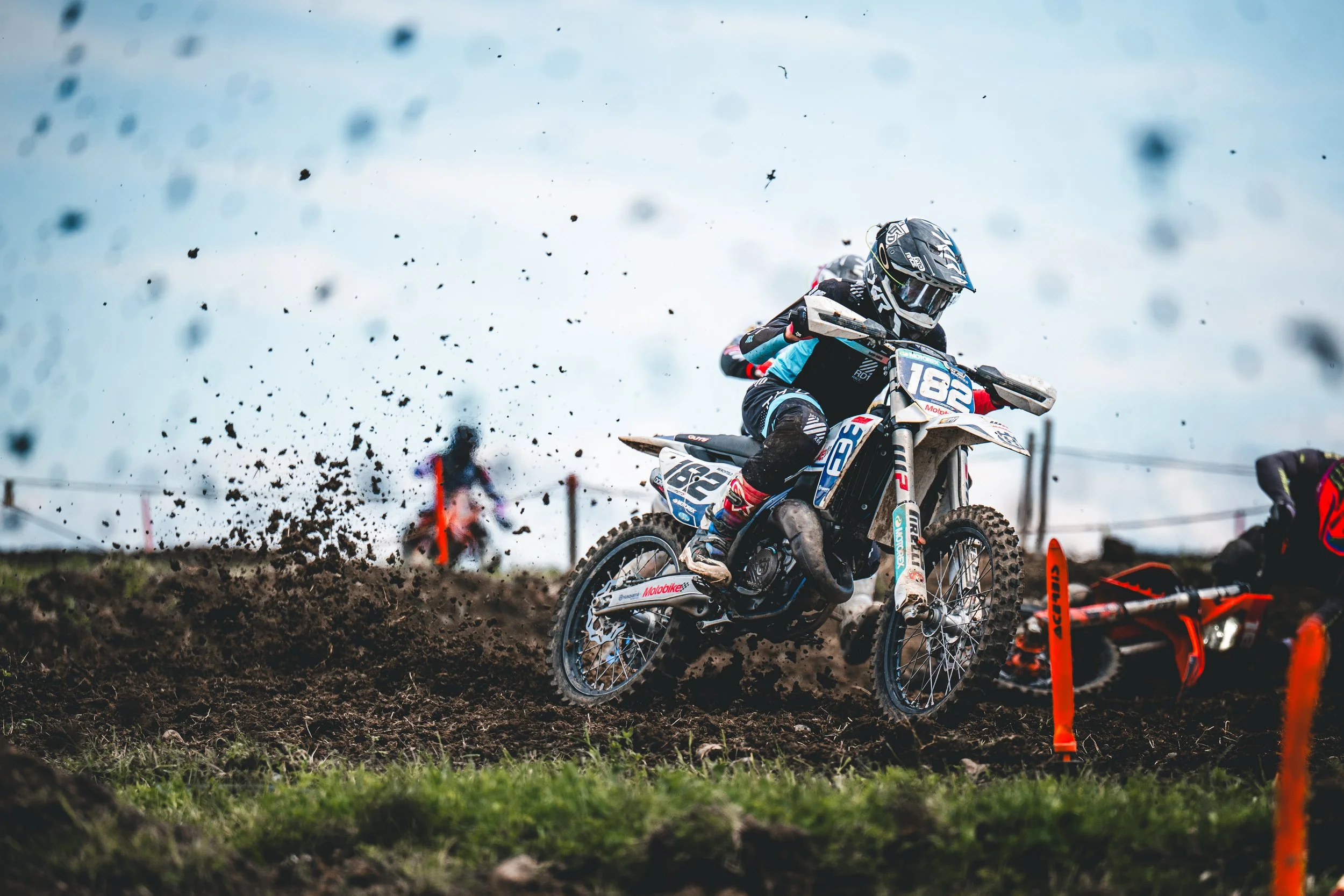 Ein Motocross-Pilot mit der Startnummer 182 auf einer Husqvarna bezwingt eine schlammige Rennkurve beim SAM-Rennen in Hünikon (Thurgau), intensive Sport-Action aus der Schweiz.