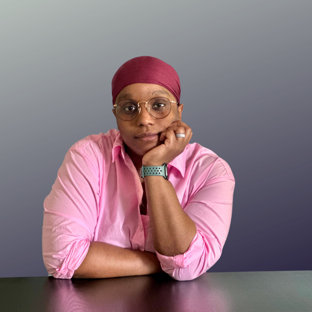 A person wearing a pink shirt, glasses, and a red headscarf, resting her face on her hand at a dark table against a gray background.