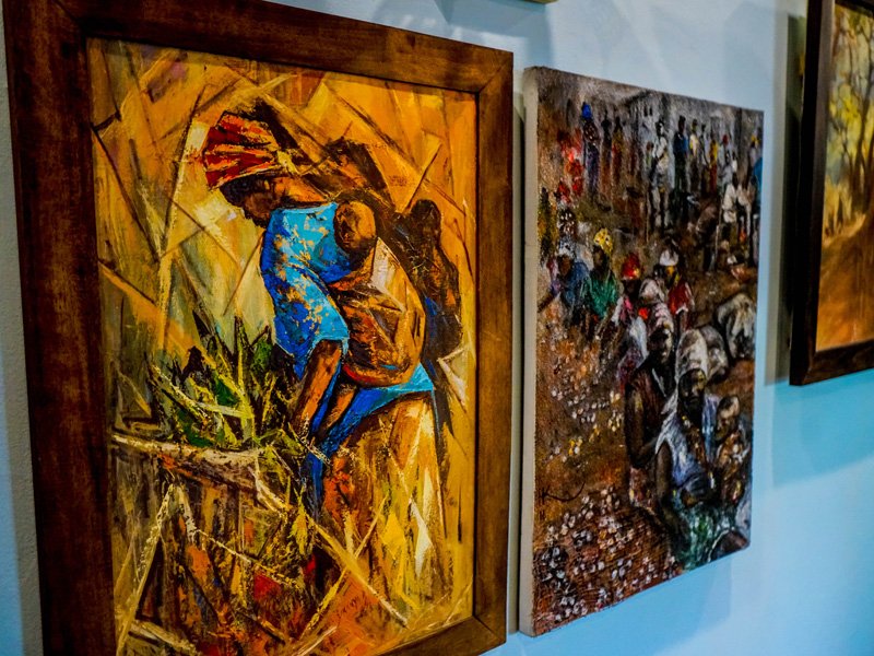 Paintings of African people, one showing a person working in a field and the other depicting a bustling marketplace scene.