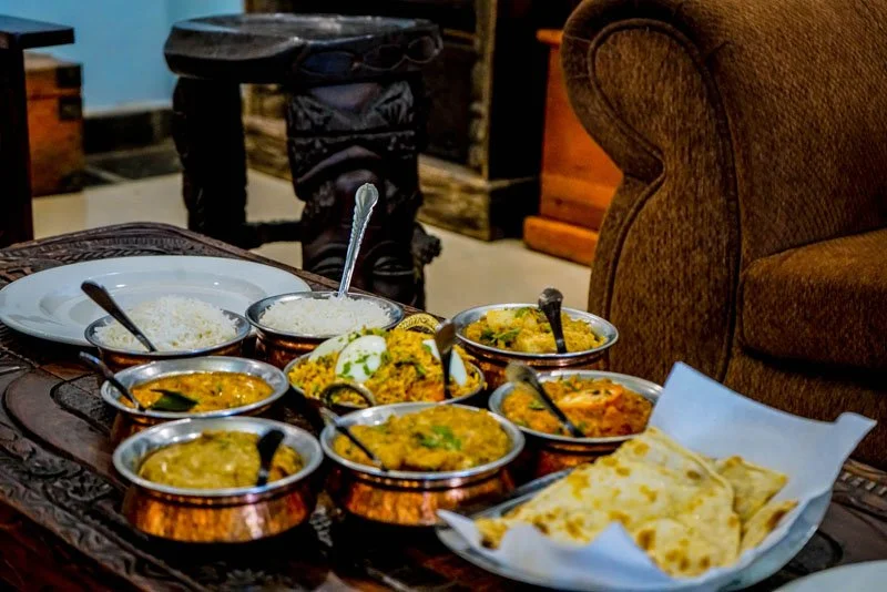 Various Indian dishes served in small copper bowls on a wooden table, including curries, rice, and naan bread.