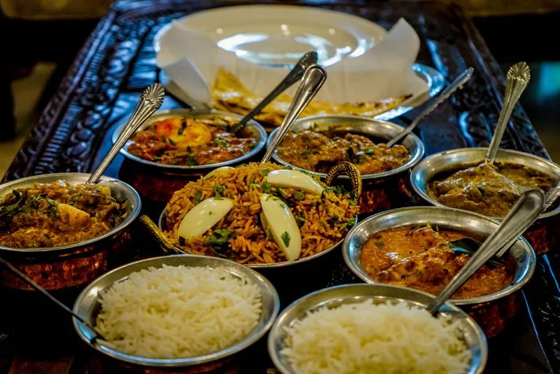 Assorted Indian dishes including rice, curries, and vegetables served in metal bowls on a wooden table.