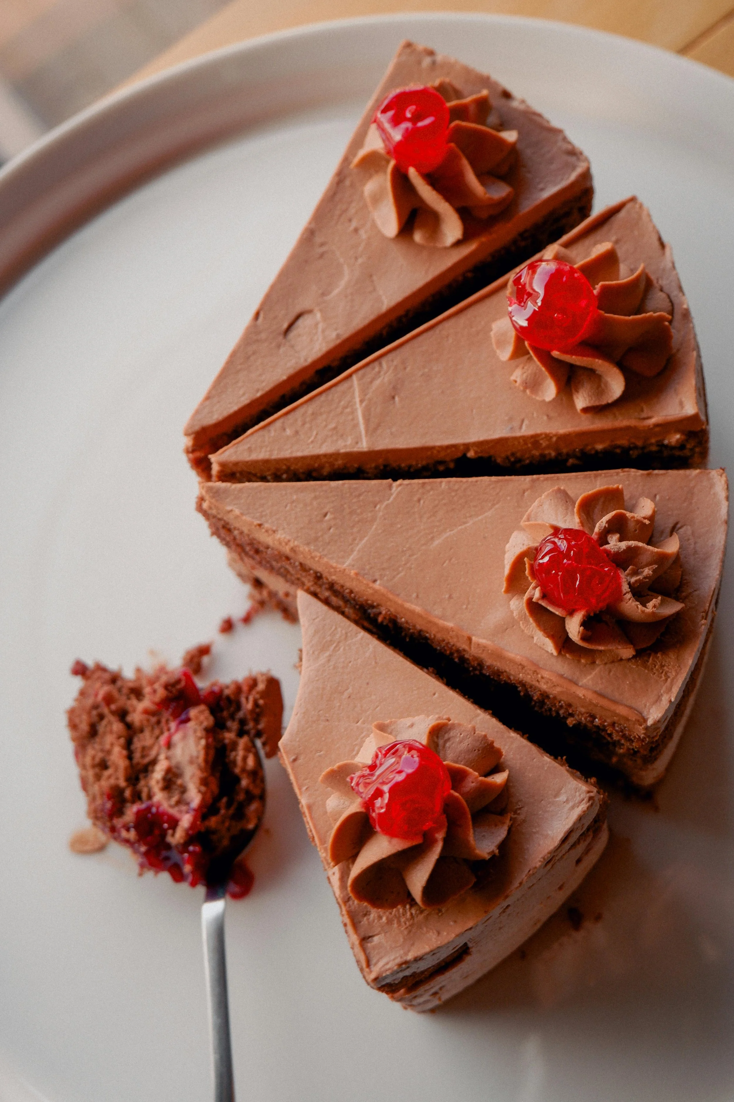 Chocolate cake slices with whipped frosting and cherry toppings on a white plate