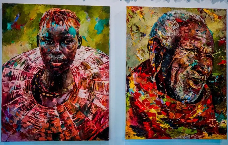 Two colorful paintings of African individuals, one of a young woman with short hair and traditional jewelry, and the other of an older man with a beard, both with vibrant backgrounds.