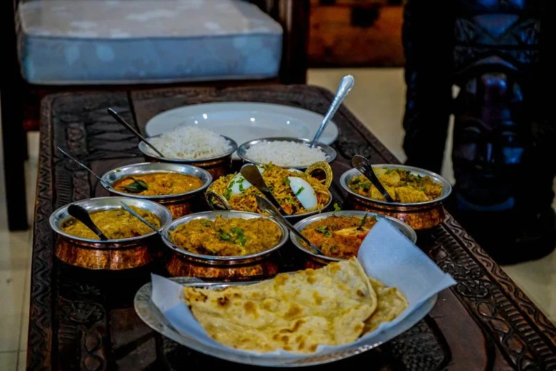 Spicy Indian curry dishes, rice, and naan bread on a wooden table in a restaurant.