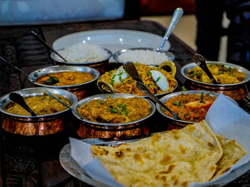 Assorted Indian dishes including rice, naan bread, and various curries in copper bowls.