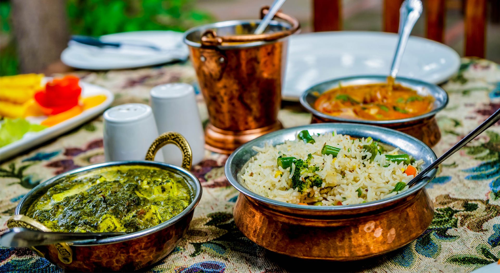 Indian meal on a table with rice, curries, and vegetables on a decorative tablecloth.