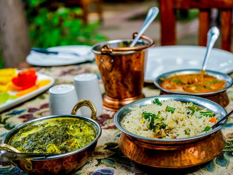 Indian meal featuring rice, curry, and vegetables served in copper bowls on a decorated table.