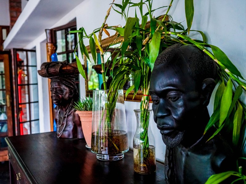 Decorative interior with dark wooden bust sculptures of African figures, potted plants, and glass vases on a black table near windows.