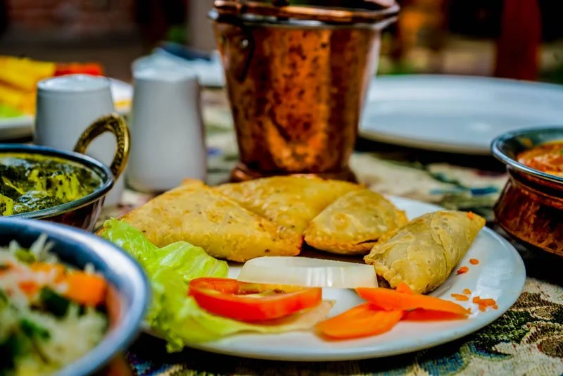 Plate with stuffed flatbreads, lettuce, tomato slices, and onion slices, surrounded by various bowls and cups of sauces and drinks on a patterned tablecloth.