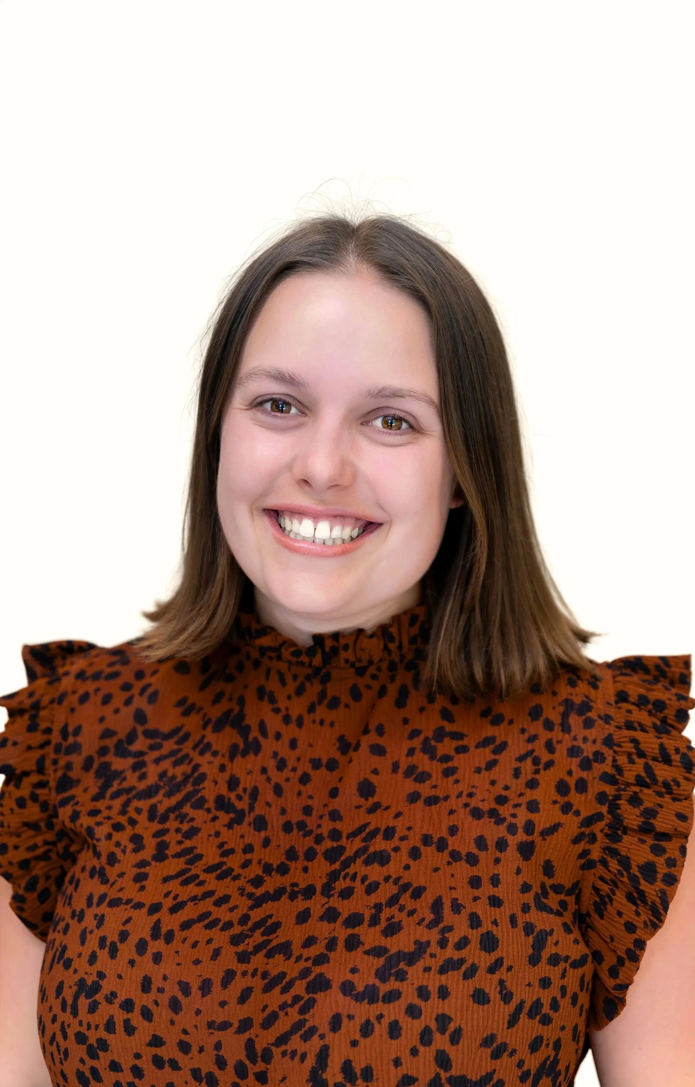 A woman with long brown hair, smiling, wearing a navy blue sweater, against a plain background.