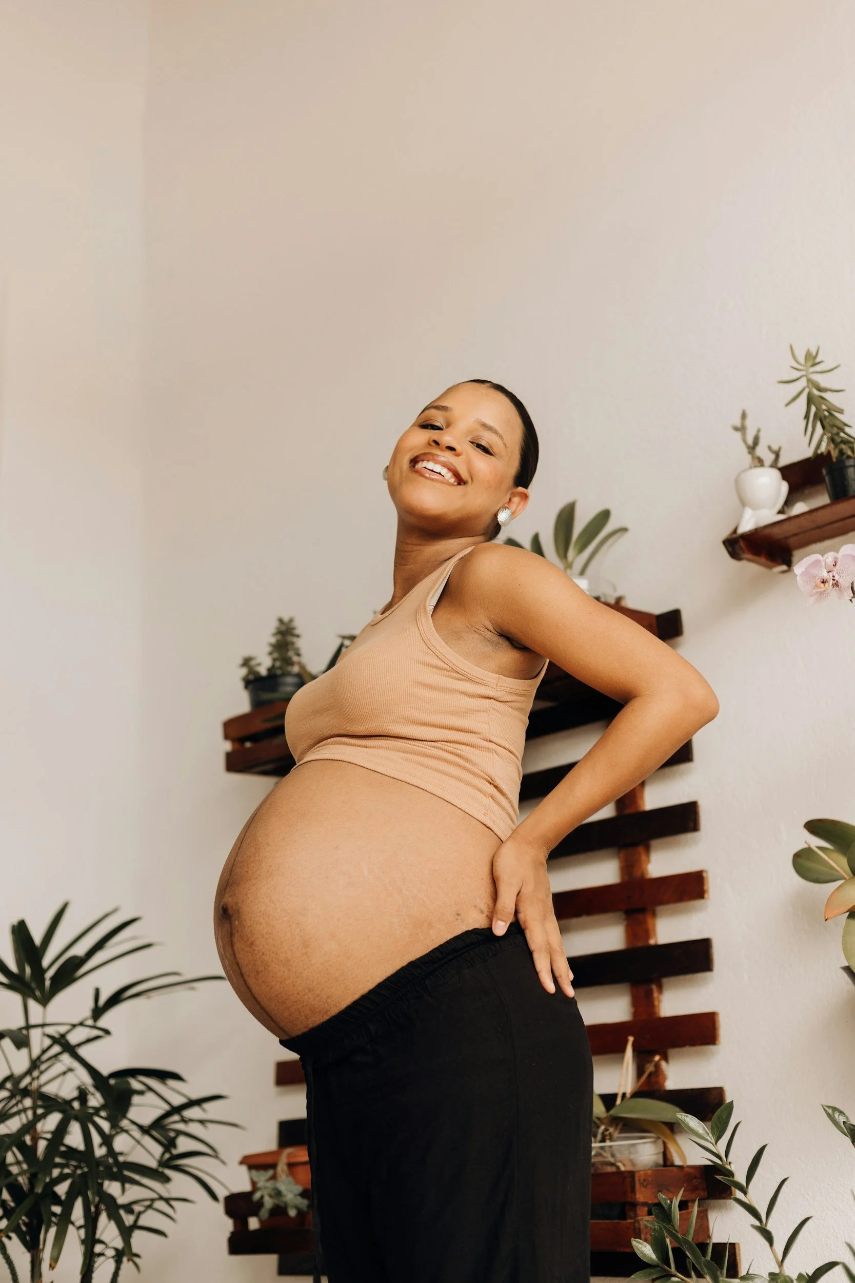 A smiling pregnant woman stands in a welcoming home environment, reflecting comfort and confidence during pregnancy.