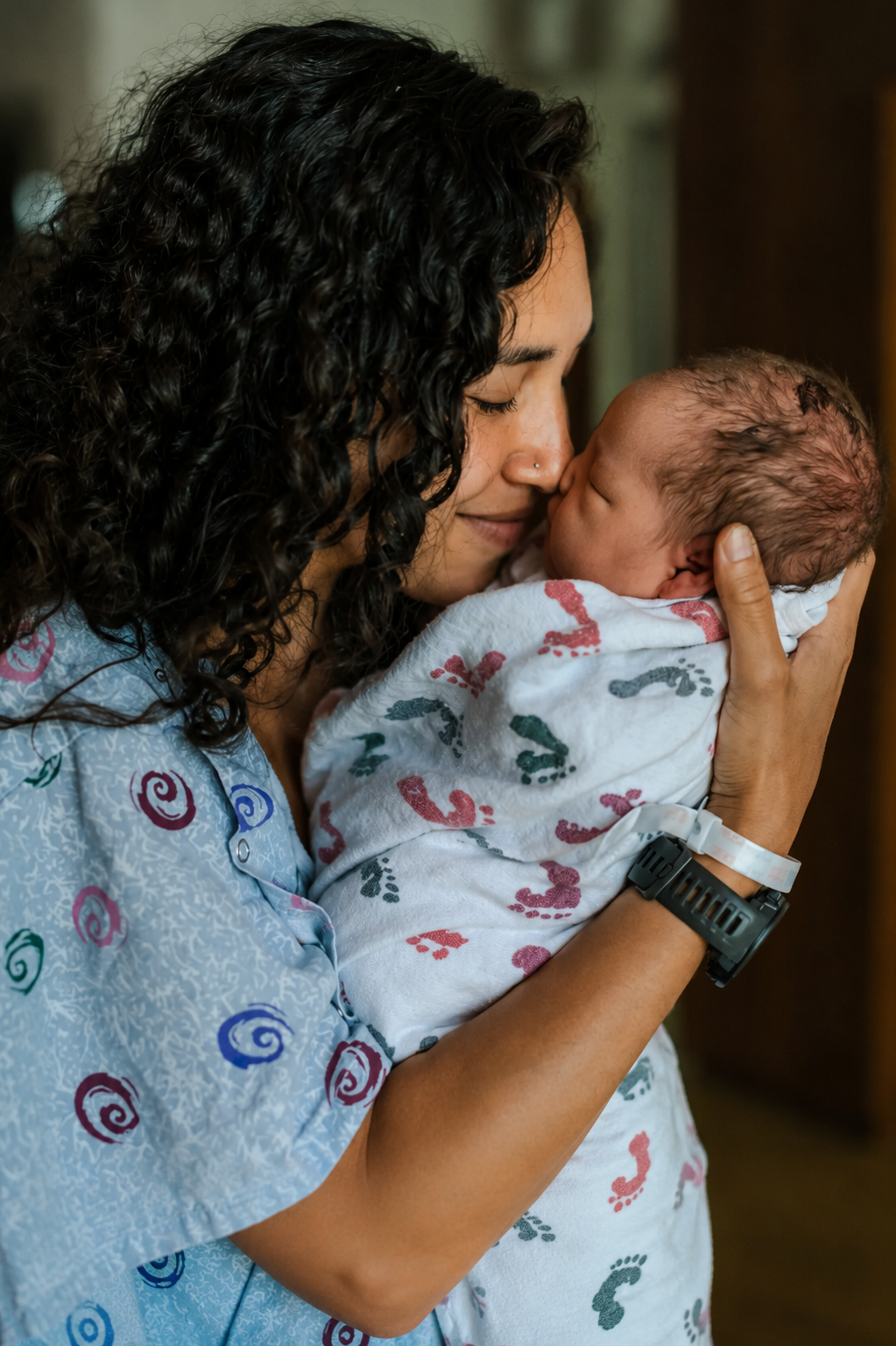A woman with curly black hair holding a young child in a bright orange dress inside a modern kitchen.